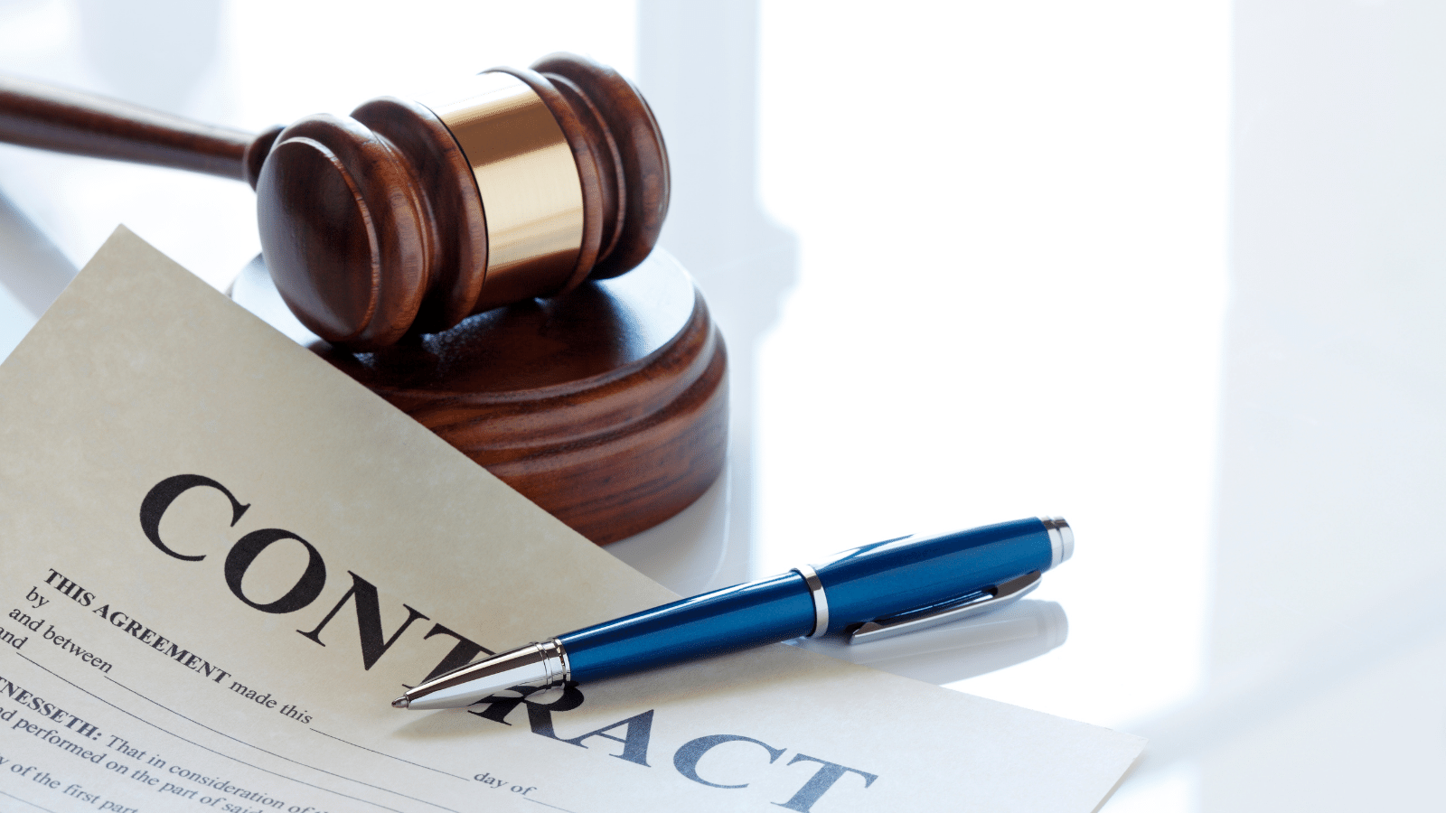 Image of a contract with a blue pen laying across the top of it, situated next to a gavel and a sound block