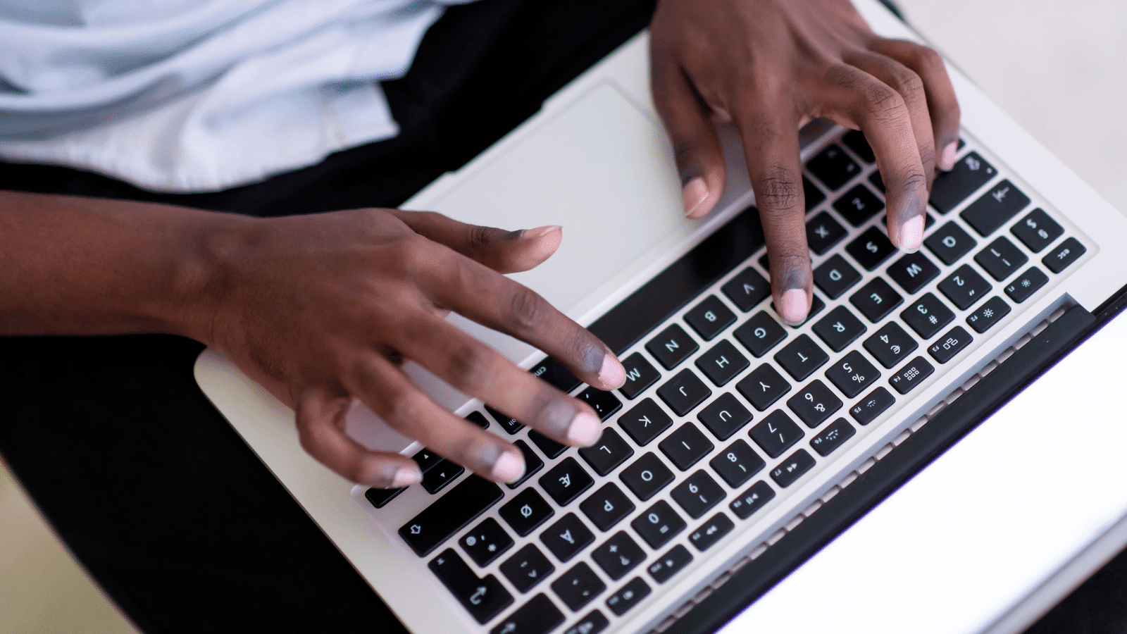 black person sitting with his laptop on his lap, typing